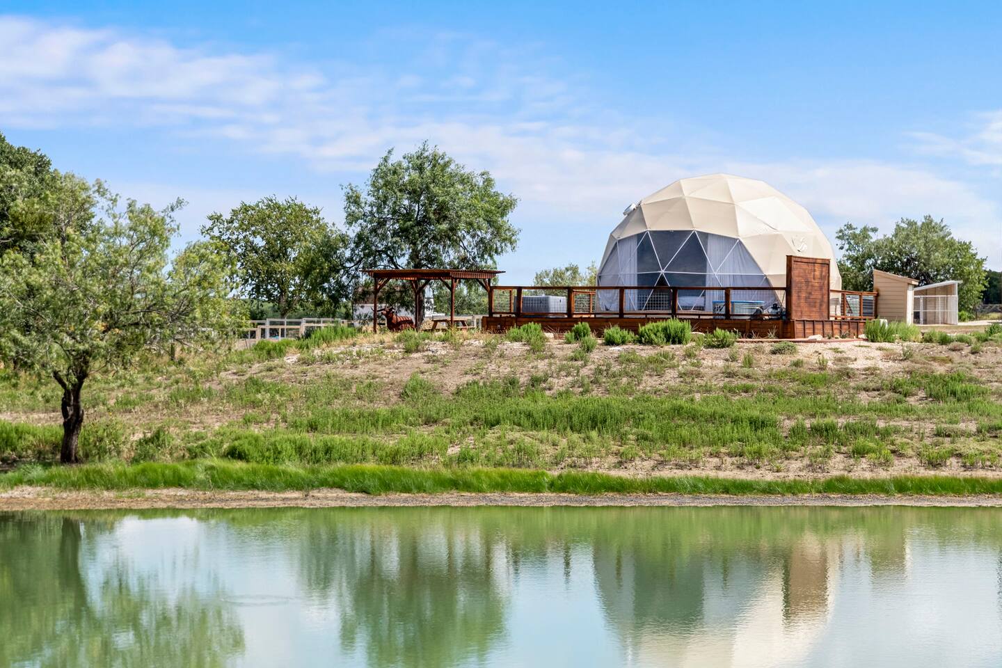 The Haven glamping dome with panoramic windows and deck reflected in the pond at The Farm Texas